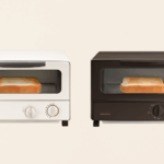 象印トースターEQ-SB22-BW（ホワイト）とEQ-AH22-BZ（ブラウン）を並べて比較した画像。両機種とも庫内にトーストが1枚入っており、外観デザインや焼き加減の違いがわかる構成。