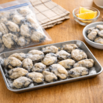 木目のキッチンにトレーと袋の上で並べた冷凍牡蠣のむき身｜家庭用1kg冷凍牡蠣の量と使いやすさがわかる写真